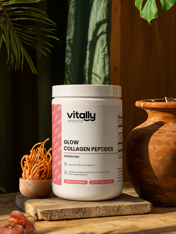 A white tub of Vitally Essential Glow Collagen Peptides sits on a stone slab in a styled setting with warm sunlight, a terracotta pot, dried herbs, and green leaves in the background.