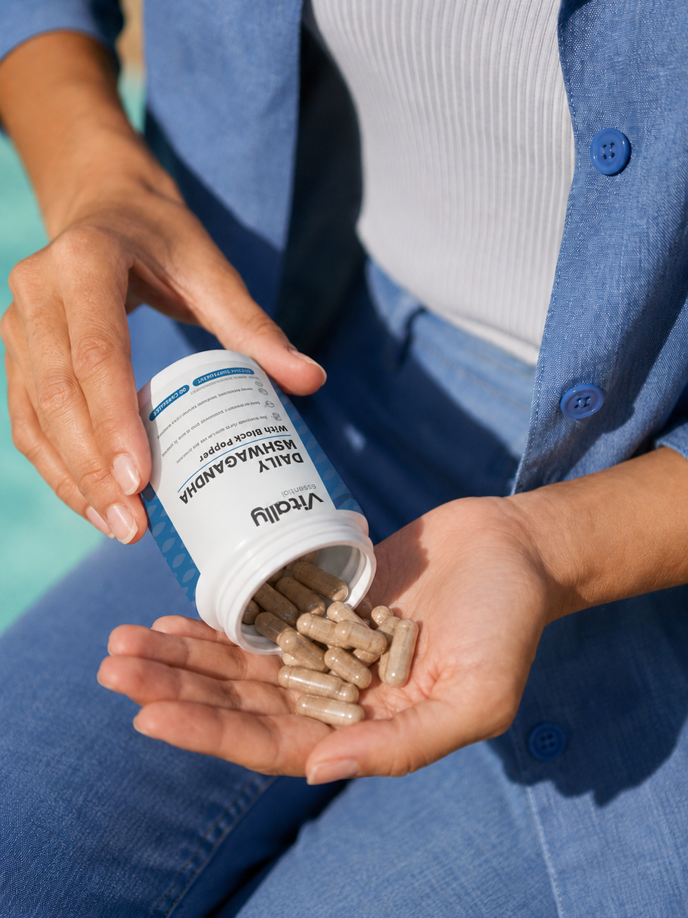 A white plastic bottle of Vitally Essential Daily Ashwagandha dietary supplement with black pepper, featuring a white label with blue accents and a white cap, set against a light gray background.