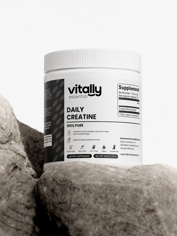 A white plastic tub of Vitally Essential Daily Creatine supplement, displayed on large gray rocks against a clean white background.