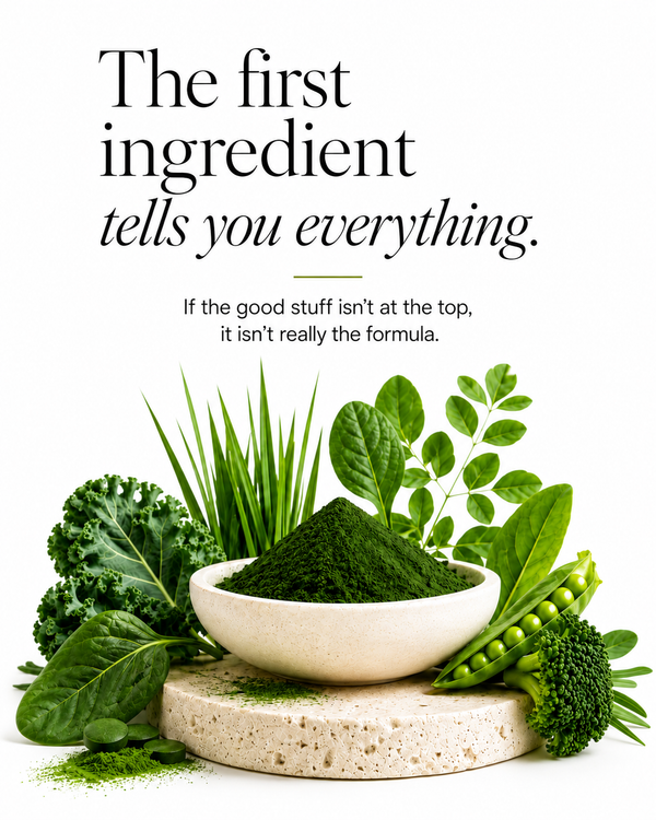 A clean white graphic with the text 'The first ingredient tells you everything.' above a styled arrangement of green vegetables and a bowl of dark green powder on a stone pedestal.