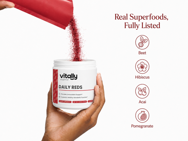 A hand holds a white tub labeled 'Vitally Essential supplements DAILY REDS' while a red scoop pours red powder into it. To the right, text reads 'Real Superfoods, Fully Listed' with icons for Beet, Hibiscus, Acai, and Pomegranate.