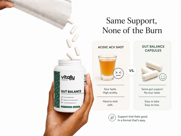 A hand holds a white bottle labeled 'Vitally Essential GUT BALANCE' while capsules pour out from an overturned white package. The right side includes marketing text comparing acid-based shots with gut balance capsules, with illustrated cups and capsules on a clean white background.